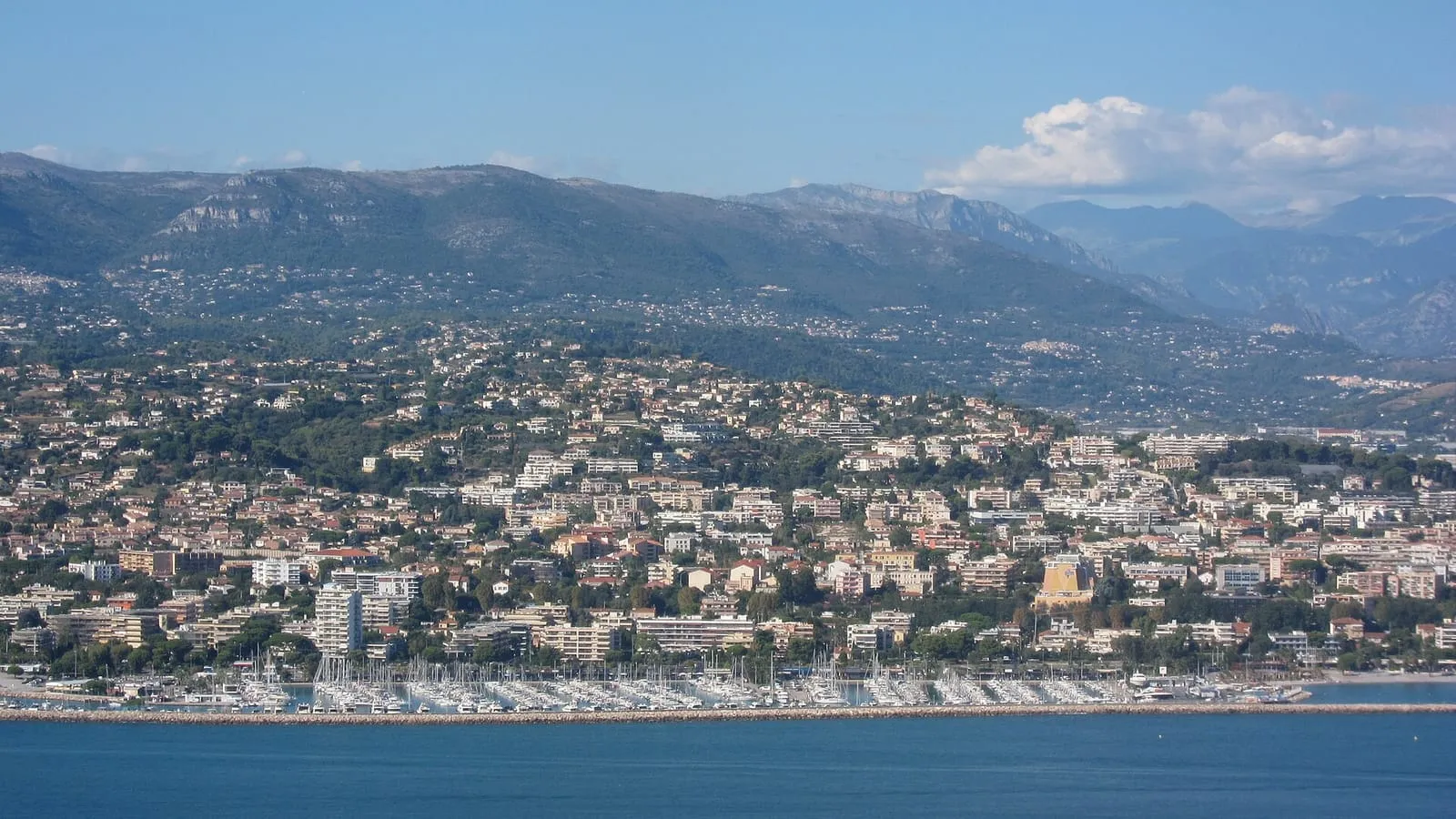 Vue aérienne de Saint-Laurent-du-Var : le port de plaisance et ses voiliers, la ville étagée sur les collines et les Préalpes d'Azur